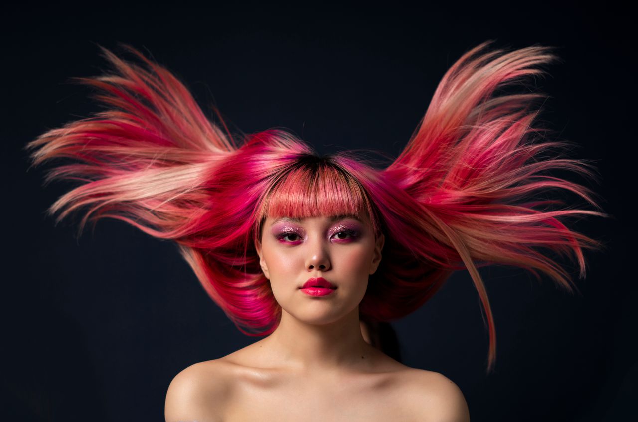 Captivating portrait of woman with vibrant pink hair against a dark background.