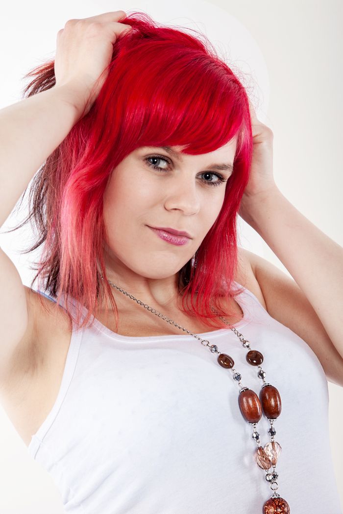 Woman with red hair in white tank top posing confidently indoors.